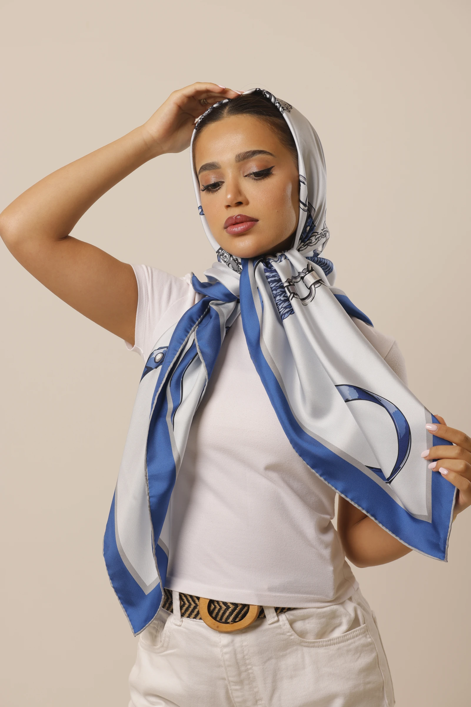 Azure Keepsake silk scarf tied over the head, with one hand raised